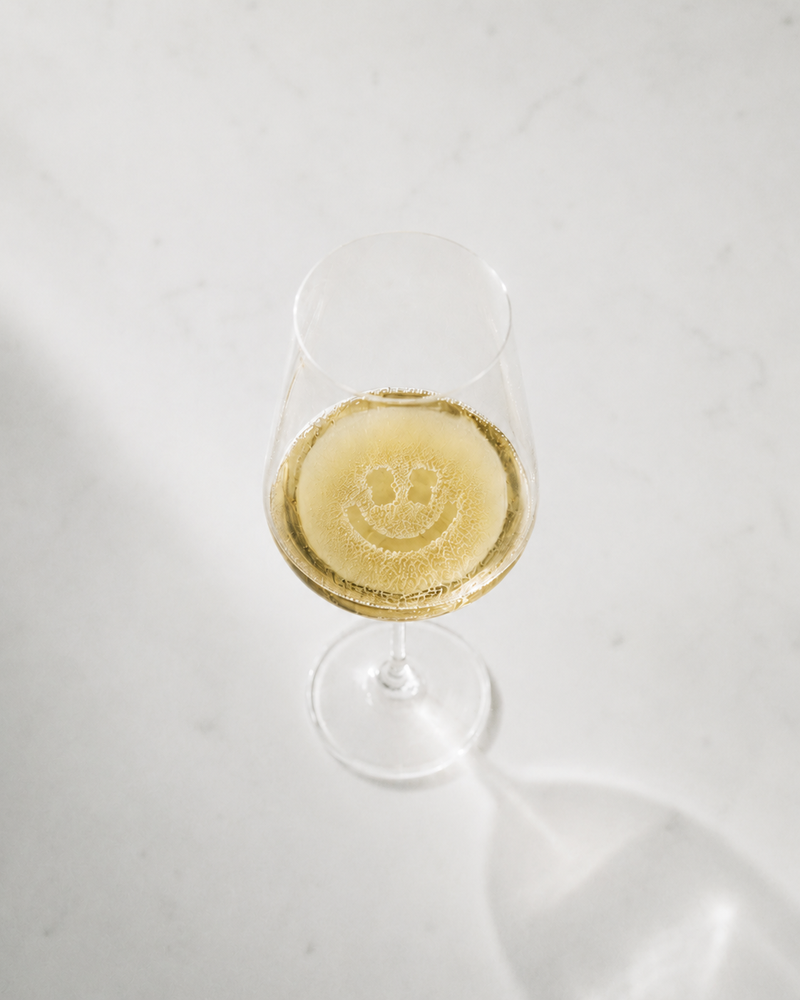 A glass of sparkling wine with a smiley etched in the foam, warm analog light